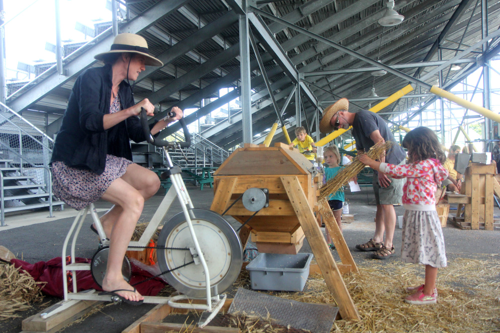 Emily Vogler of Westport, Mass., works a wheat thresher Saturday with her 4-year-old daughter, Lucia Yoder, at the annual Artisan Bread Festival at the Skowhegan fairgrounds.