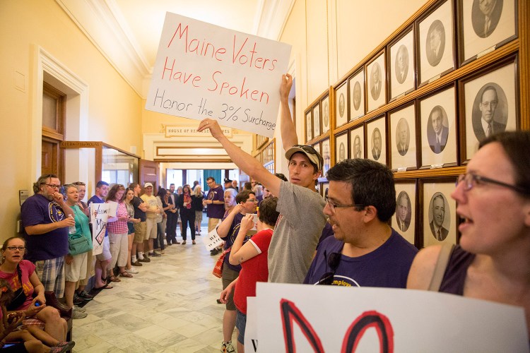 In a protest at the State House on July 3 – the third day of the state government shutdown –
 Tom Gilbert of Topsham holds up a sign in favor of the voter-approved 3 percent tax surcharge on the state's highest earners. Later that day, the Legislature passed a budget that dropped the surcharge. 