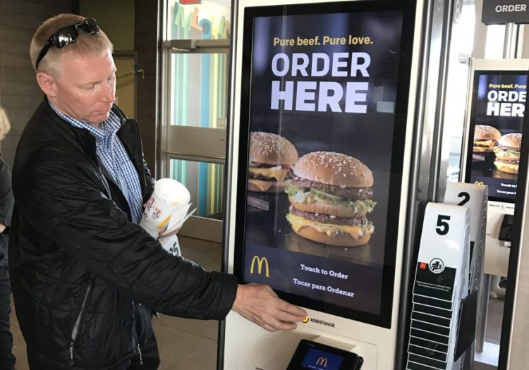 Gorham Road McDonald's owner James Nygren demonstrates functions on a new ordering kiosk last year. The writer says the objection that fast-food restaurants are built on a soulless factory model is a facile argument, and obscures the genius behind the phenomenon.