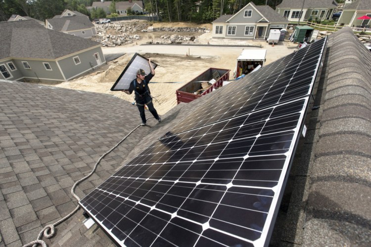 Jack Doherty, photovoltaic project manager for ReVision Energy, carries a solar panel to the roof ridge of a home at OceanView at Falmouth. Though there's frustration, "facts do matter and they will eventually prevail," said James Cote, a lobbyist who represents an alliance of solar installers.
