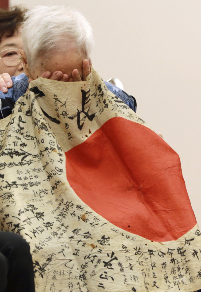Sayoko Furuta, 93, reacts as she is covered with the Japanese flag that her brother brought to battle in the South Pacific.