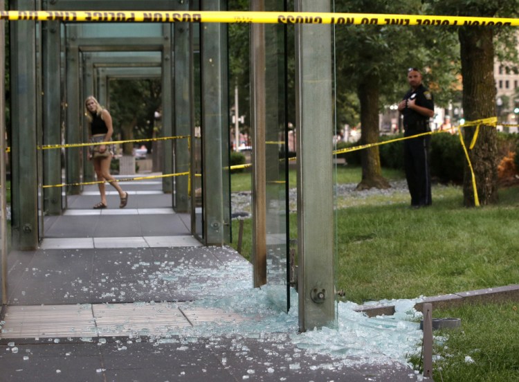 A passerby and a Boston police officer stand Monday near broken glass at the New England Holocaust Memorial. It was the second time the memorial has been damaged this summer.