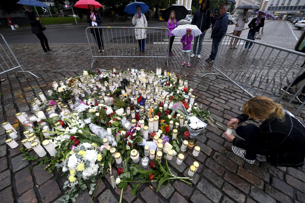 A woman places a candle Saturday by floral tributes to the victims of a stabbing attack in Turku, Finland, on Friday that killed two people.