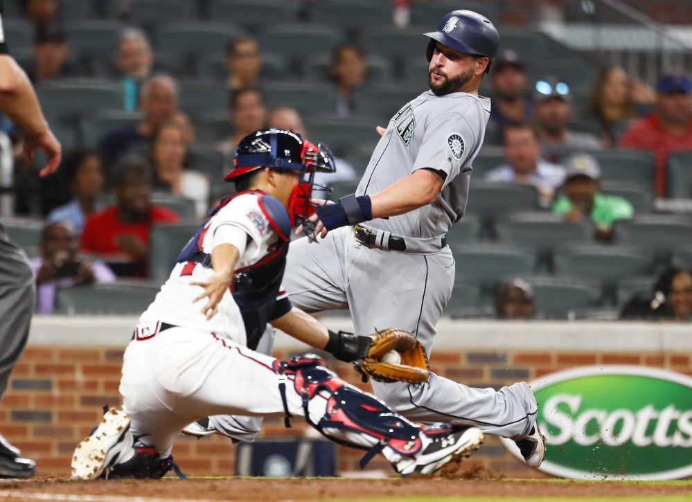 Yonder Alonso of the Mariners avoids the tag of Braves catcher Kurt Suzuki to score in the fourth inning Monday night in Atlanta. Seattle, which began the day 1 game out of a wild-card spot, won 6-5.