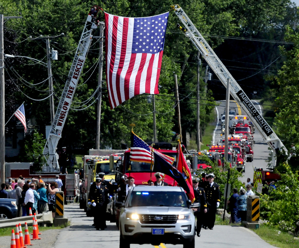 A memorial service procession of area fire departments makes its way Sunday under an American flag en route to the China Village fire station to honor the late former Fire Chief George Studley.