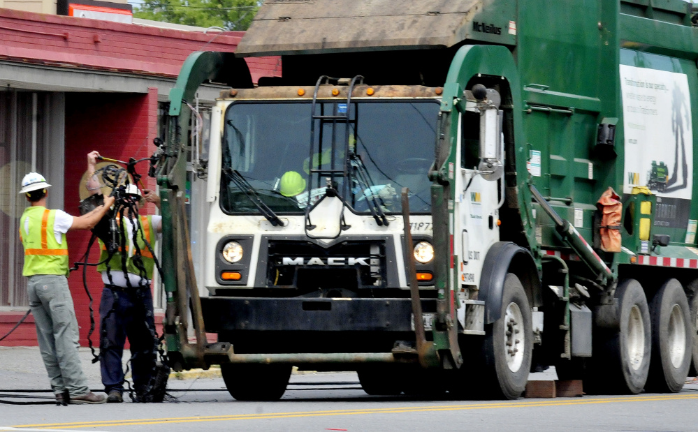 Workers pull a coil of wires off the hydraulic lifts of a Waste Management truck after the truck struck wires hanging low across College Avenue in Waterville on Tuesday. Police believe another truck snagged the wires and left the scene causing them to hang lower than usual and then the Waste Management truck hit the wires.