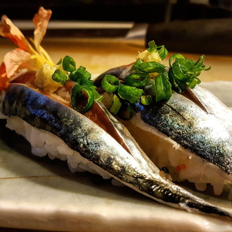 Two pieces of mackerel nigiri topped with ground ginger and scallions.