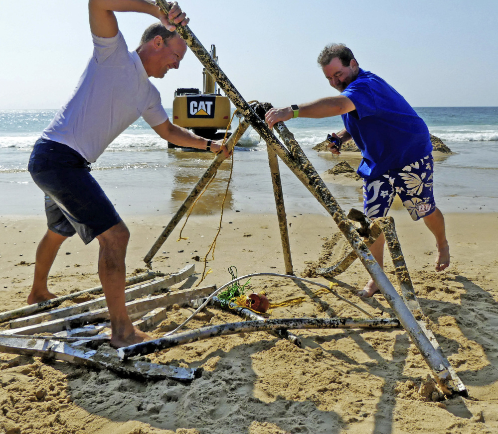 Peter Brockmann, left, president of the East Beach Association, gets help assembling pieces of a mystery object removed from the surf Thursday.