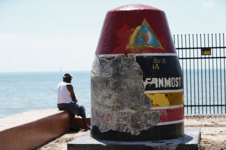 A man fishes Wednesday next to Key West's Southernmost Point Buoy, which shows damage done by Hurricane Irma.