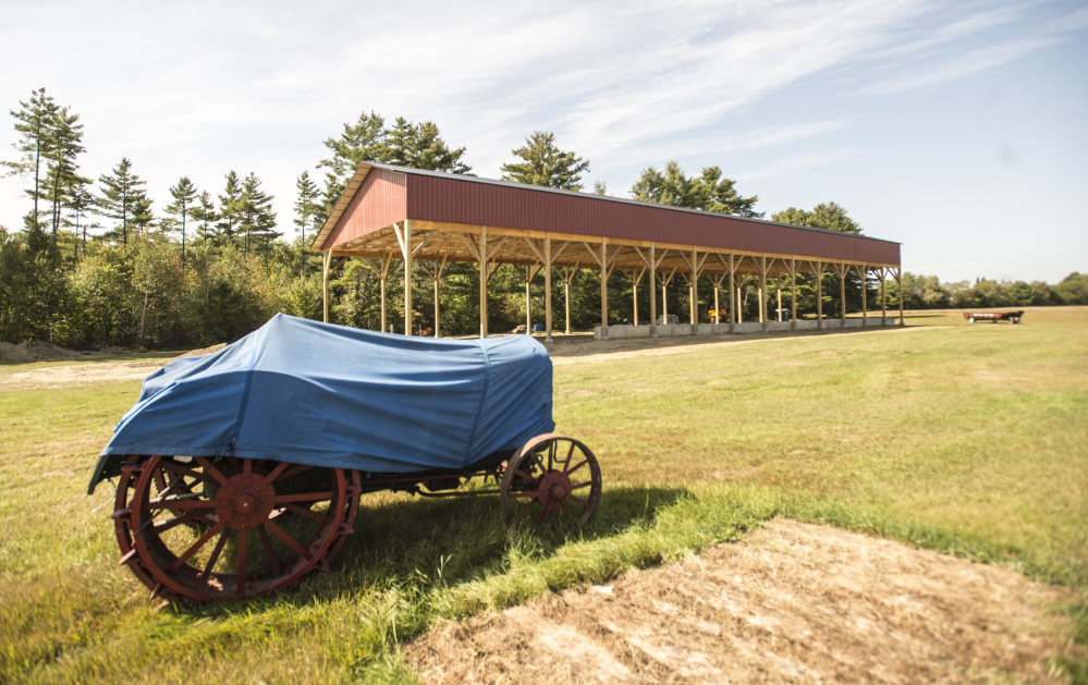 An antique tractor protected by a tarp stands at the Maine Antique Tractor Club in Norridgewock next to the new tractor-pull building built by an Amish construction company.