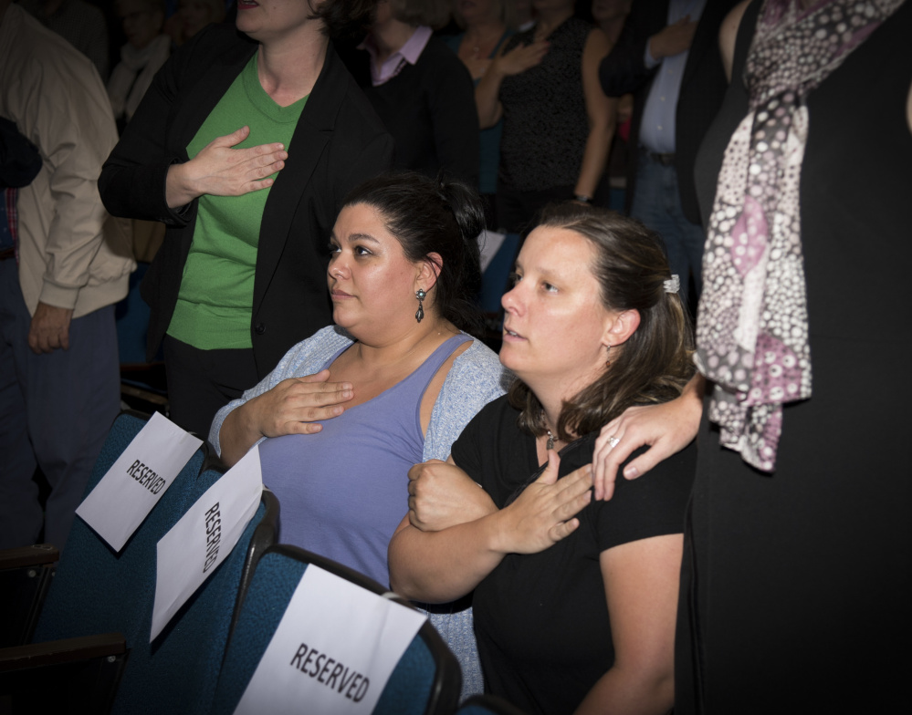 April Fournier, left, and Liz Smith kneel while reciting the Pledge of Allegiance at the opening of a Democratic gubernatorial candidates' forum Thursday evening at the University of Maine at Augusta. Zak Ringelstein led the Pledge of Allegiance and invited attendees to stand or kneel.