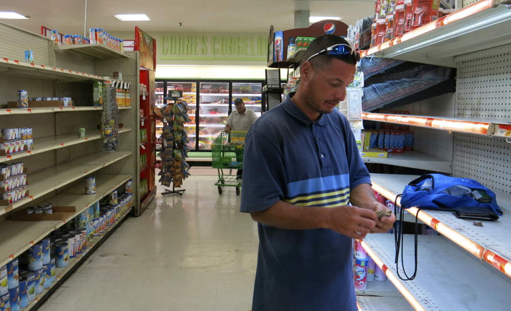In this Monday, Sept. 25, 2017 photo, Christian Mendoza counts money in the aisle of a supermarket where he had hoped to buy bottled water but only found cans of juice, in San Juan, Puerto Rico. Mendoza said the car wash where he works hasn't re-opened so he has been selling bottled water, even though he isn't able to refrigerate it. (AP Photo/Ben Fox)