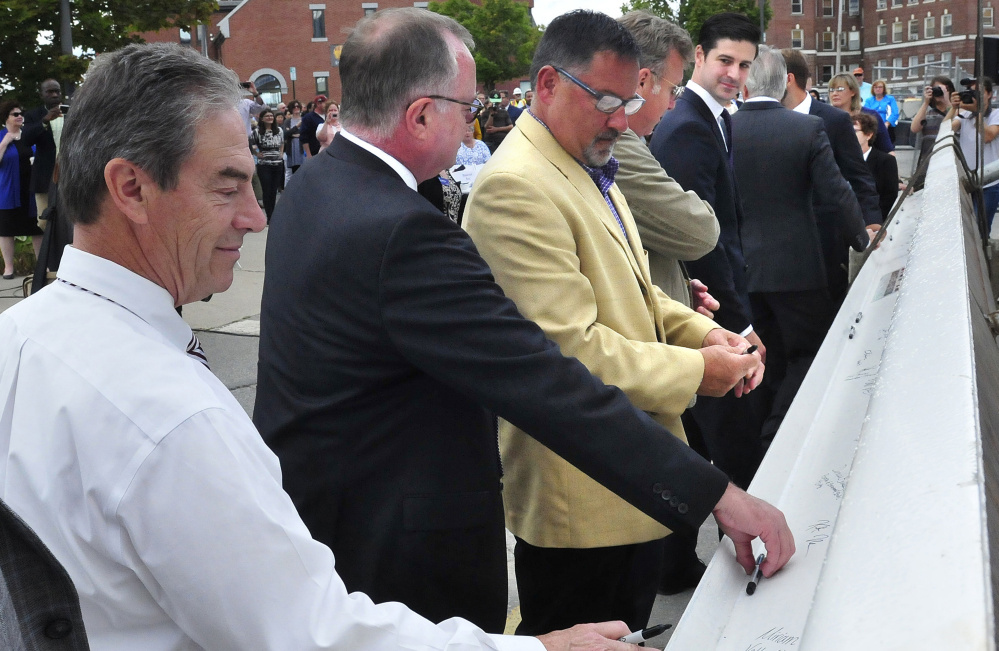 Waterville City Manager Mike Roy, left, and Mayor Nick Isgro, far right, join Colby College officials and builders signing the final beam on the college's $25.5 million downtown dormitory Thursday on The Concourse in Waterville.