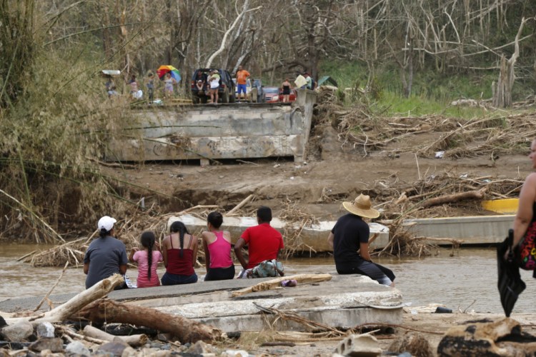 People sit Wednesday on both sides of a destroyed bridge that crossed the San Lorenzo de Morovis River in Morovis, Puerto Rico. Maria has thrown Puerto Rico's already messy economic recovery plans into disarray.