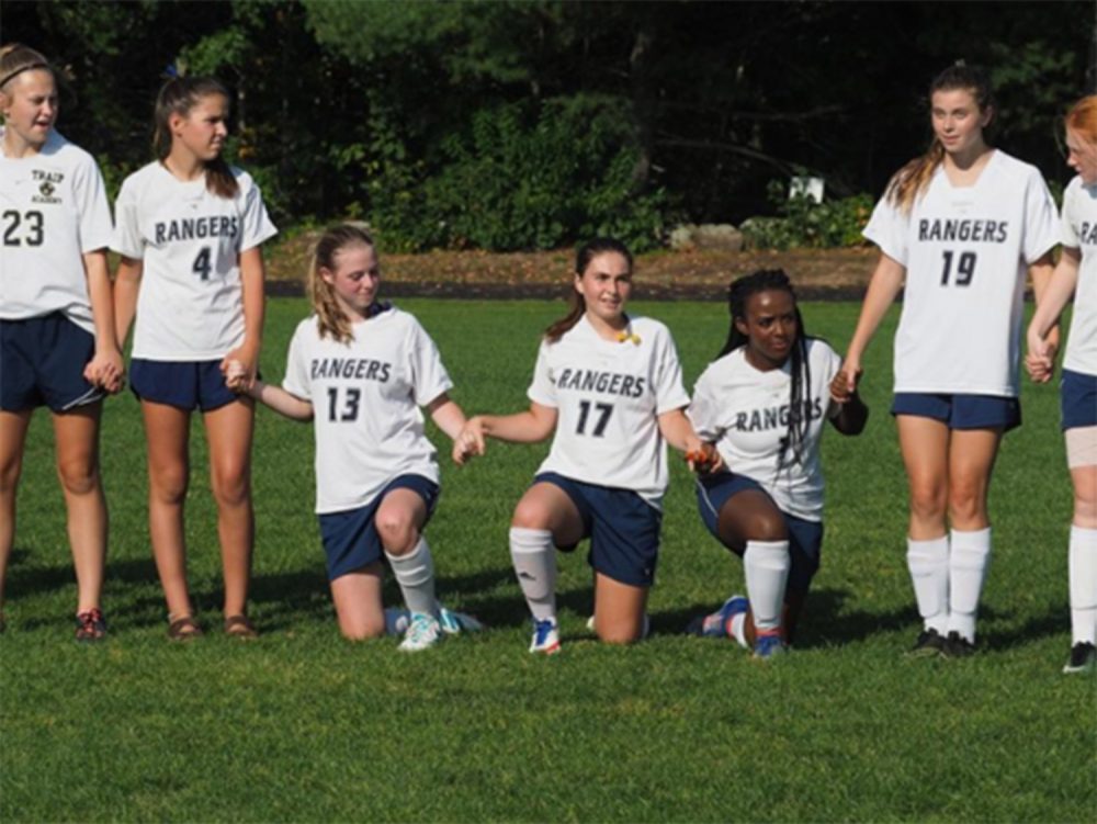 Members of the girls' soccer team at Traip Academy in Kittery take a knee during the playing of the national anthem Monday night. 