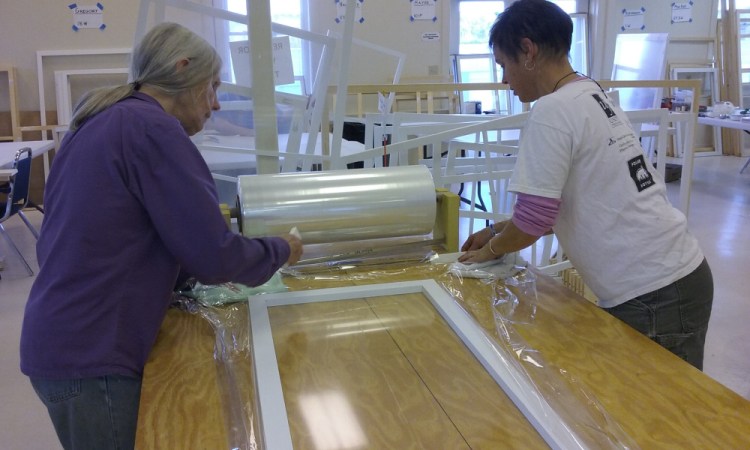 Barbara Kile and Liza Wheeler work with plastic and foam weather stripping to create an insulated window insert.