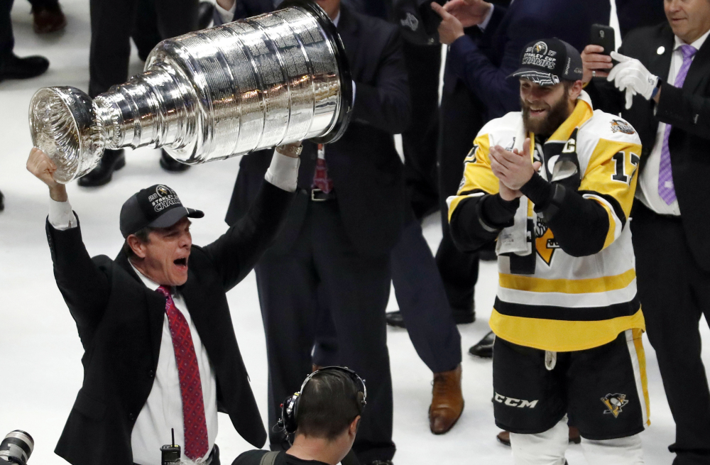 Penguins Coach Mike Sullivan hoists the Stanley Cup as Bryan Rust watches after Pittsburgh beat Nashville in Game 6 on June 11 to win the title. Sullivan challenged his players to 'three-peat' even while they were celebrating a second straight Cup.