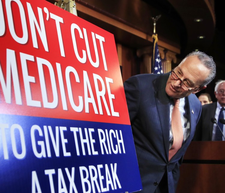 Senate Minority Leader Chuck Schumer of New York looks at a poster at the start of a news conference on Capitol Hill.