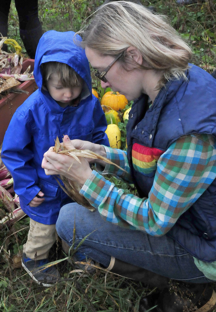 Cate Jacques shows her son Theodore corn grown using the Three Sisters technique of planting corn, squash and beans in a single mound, during an Indigenous Peoples Day celebration at the Sweet Land Farm in Starks on Monday.