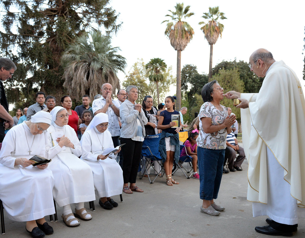 From a retrofitted trailer pulled by a truck, Bishop Armando X. Ochoa of the Roman Catholic Diocese of Fresno, Calif., gives Communion during a Mass at Kearney Park in Fresno as part of the diocese's 50th anniversary in September.