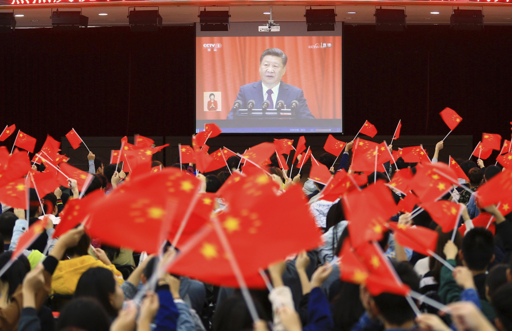 Students wave flags Wednesday as they watch a televised speech by President Xi Jinping during the opening ceremony of China's twice-a-decade party congress in Huaibei.