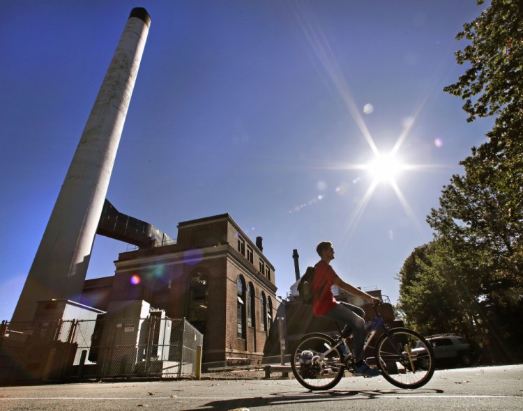 A student cycles past the UNH Cogeneration Facility last week at the University of New Hampshire in Durham. The school won prestigious recognition for having a campus powered entirely by renewables and recycling up to 25,000 pounds of food each month.