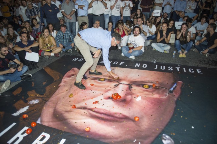 A banner with a photo of Malta Police Commissioner Lawrence Cutajar is on the floor outside the Malta Police Headquarters as people throw coins, tomatoes and cheesecakes at it and at the facade during a rally to honor anti-corruption reporter Daphne Caruana Galizia, killed by a car bomb on Oct. 16, in Valletta, the capital city of Malta, on Sunday.