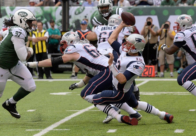 Tom Brady throws a pass while falling to the turf as Jets defensive end Ed Stinson closes in during Sunday's game. The Patriots got out with a win, but they're far from the team that some predicted would go undefeated this year.