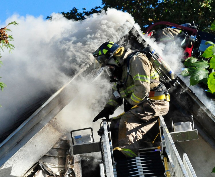 A firefighter on a ladder truck gets set up to pour water on the smokey roof of a home destroyed by fire at the corner of Main Street and Peltoma Avenue in Pittsfield on Sunday. Photo by David Leaming/Morning Sentinel