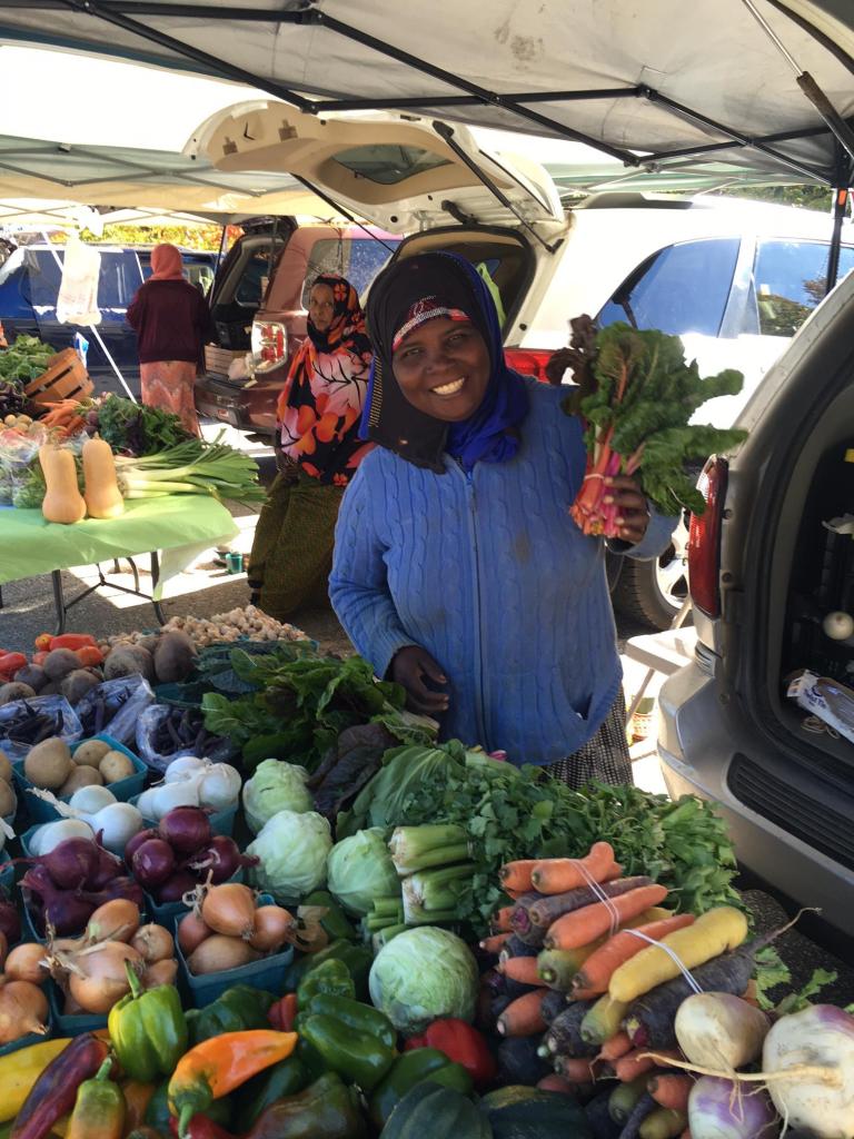 Habiba Noor offers Swiss chard from among her vegetables for sale at the Beyond Borders Farmers Market at the Viles Arboretum in Augusta. In the background is Hawa Ibrahim, who is also a farmer and a market vendor.
