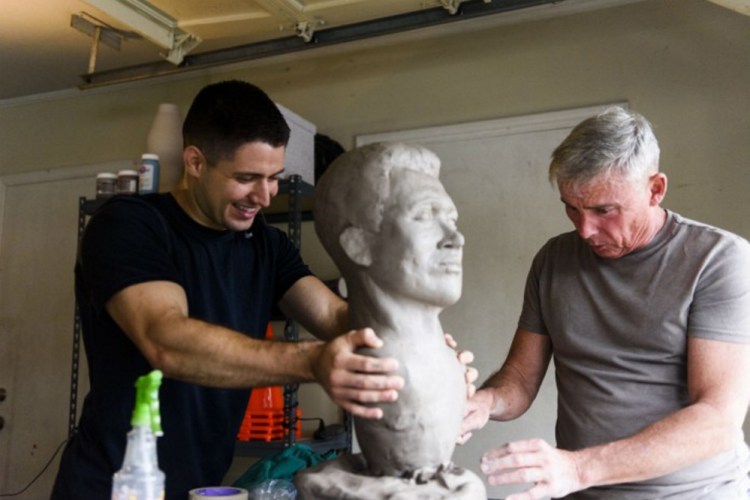 Steven Arango holds the bust of Bates College graduate George "Alexi" Whitney, while artist and retired Marine Col. Lee Busby of Alabama works on the details.