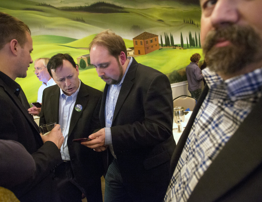 Entrepreneur Shawn Scott, center left, looks at the phone of Yes on 1 campaign press secretary Michael Sherry during a gathering of York County casino supporters Tuesday evening at Bruno's Restaurant in Portland.