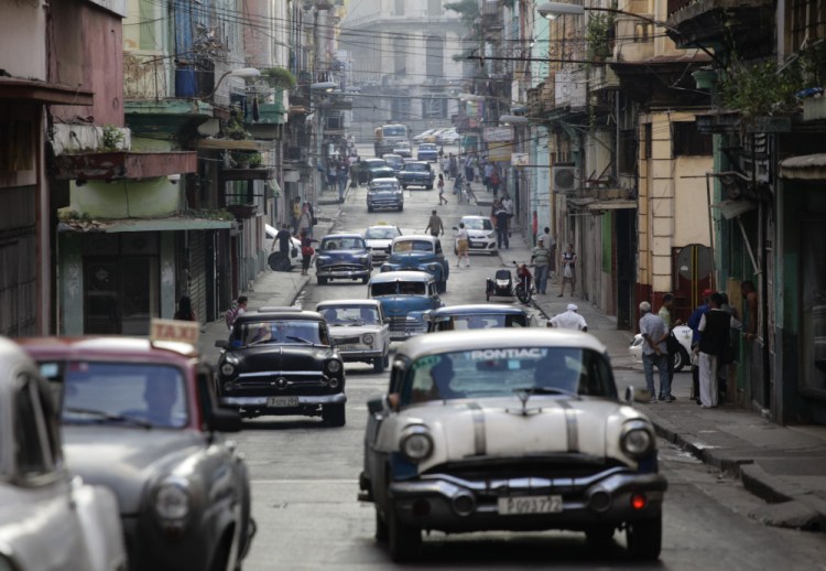 Old American cars used as collective taxis traverse a street in Havana. New restrictions on American travel to Cuba will hurt host families, guides and local farmers.
