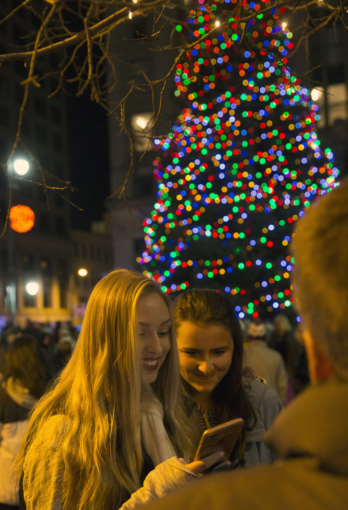 High school friends Kendra Alexander, left, and Courtney Lee check themselves out on Snapchat after the annual tree lighting in Monument Square.