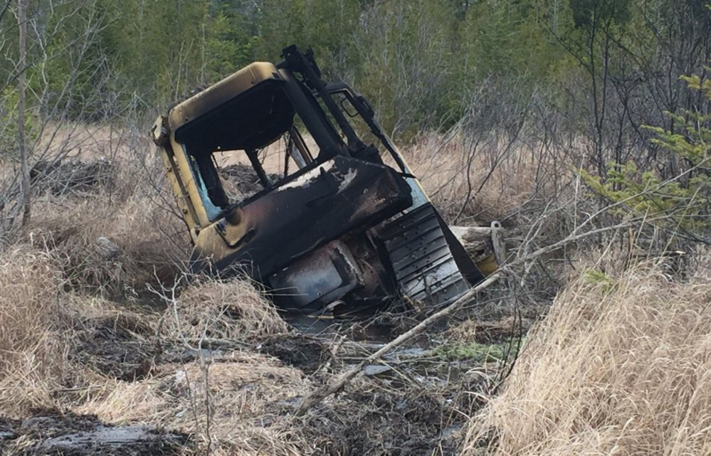 This burned bulldozer, owned by Cousineau Wood Products of Wilton, was found by hunters earlier this month off Beech Hill Road in Sandy River Plantation.Two Maine men and a Massachusetts man face arson charges.