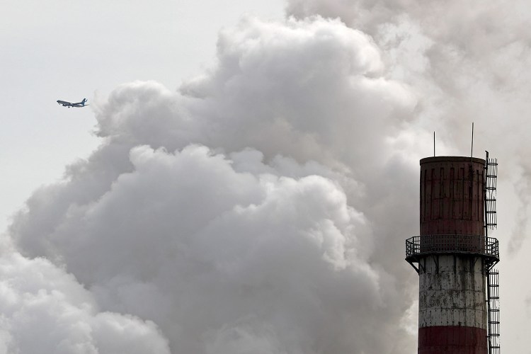 A passenger airplane flies near steam and white smoke emitted from a coal-fired power plant in Beijing. On Monday, scientists projected that global carbon pollution has risen in 2017 after three straight years when the heat-trapping gas didn’t go up at all. 