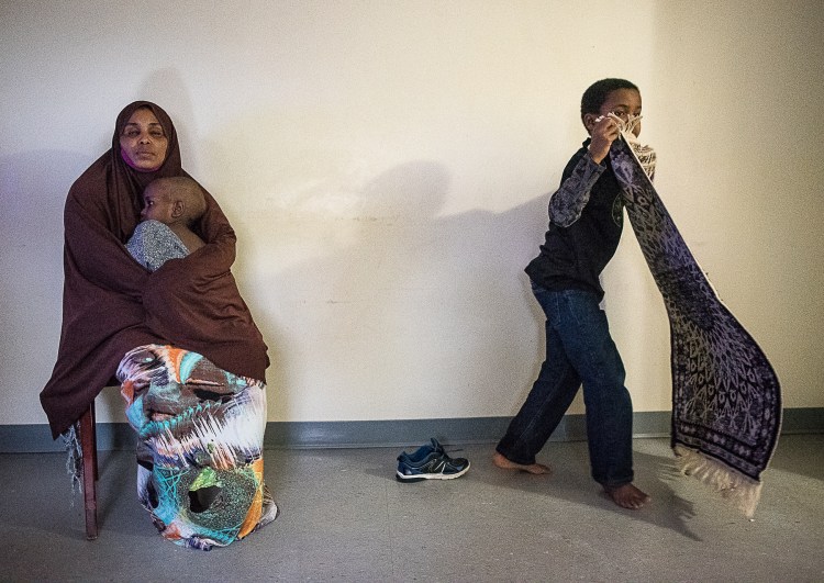 "Kadra Ahmed" sits in her living room in Lewiston with her 2-year-old son, who was diagnosed with lead poisoning while living at their former apartment. Her 9-year-old son picks up his prayer rug. "All our life is dependent on his sickness," Ahmed said through an interpreter. "Our life is just changing." 