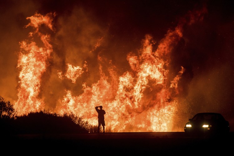 A motorist on Highway 101 watches flames from the Thomas fire leap above the roadway north of Ventura, Calif., on Wednesday.  As many as five fires have closed highways, schools and museums, shut down production of TV series and cast a hazardous haze over the region. 