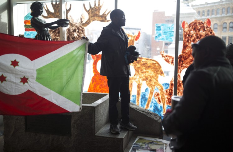 Philemon Dushimire holds up the Burundian flag Saturday as he talks to protesters inside the Portland Public Library after their demonstration in Monument Square. A group of about 25 to 30 people protested relocation of a high-ranking Burundian official's family in Maine.