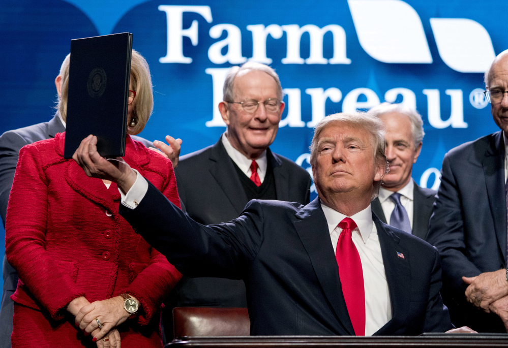 President Trump holds up a signed executive order and a memo on expanding rural broadband access at the farm bureau convention in Nashville. "In every decision we make, we are honoring America's proud farming legacy," he said.
