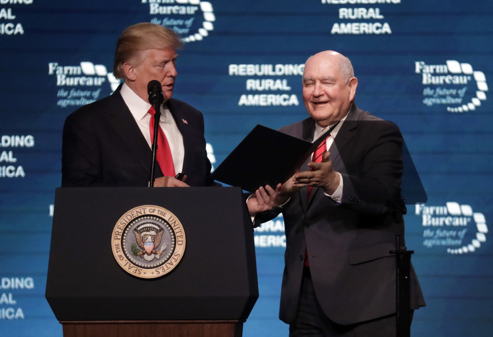 President Donald Trump hands an executive order to Secretary of Agriculture Sonny Perdue, right, after reading it at the American Farm Bureau Federation annual convention Monday in Nashville, Tenn.