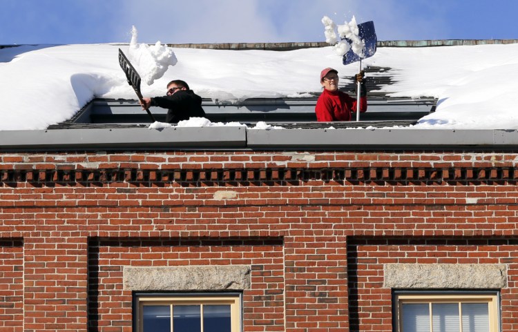 Joe Hebert, left, and Leza Gough shovel snow Tuesday from a rooftop deck on the fifth floor of 269 Commercial St. in Portland. Additional workers on the sidewalk below were diverting pedestrians away from the falling snow.