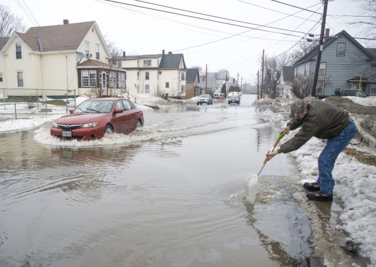 Dave Pullo, of Boston, clears a drain on Oak Street to help drain flood waters that extended down Drummond Avenue to High Street in Waterville on Saturday, Jan. 13, 2018.