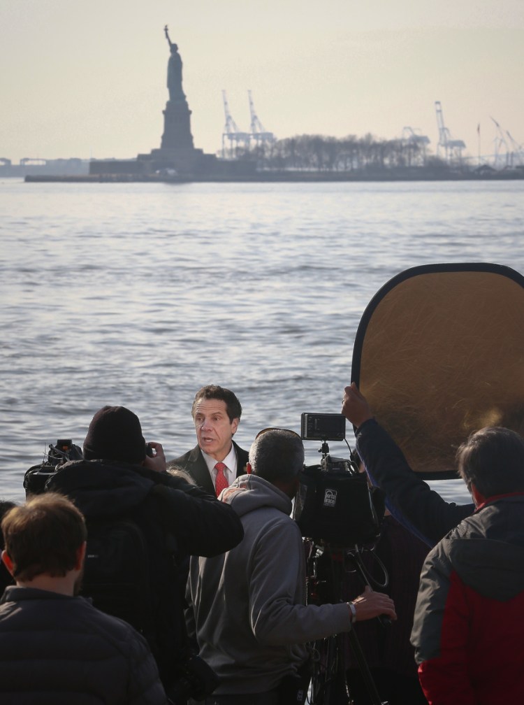 New York Gov. Andrew Cuomo, center, holds a news conference with the Statue of Liberty in the distance behind him Sunday. Cuomo says the statue and Ellis Island will be open for visitors Monday, with New York state picking up the tab for federal workers.