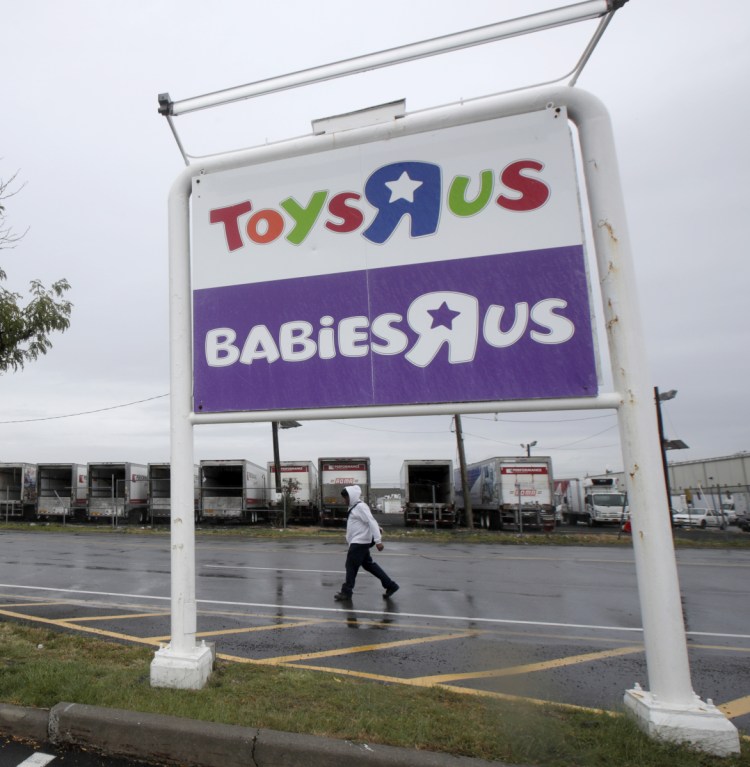 In this Tuesday, Sept. 19, 2017, photo, a pedestrian walks near a sign outside of a Toys R Us and Babies R Us store, in Elizabeth, N.J. Toys R Us, squeezed by Amazon.com and huge chains like Walmart, will close 180 stores, or about 20 percent of its U.S. locations, within months, the company announced Wednesday, Jan. 24, 2018.