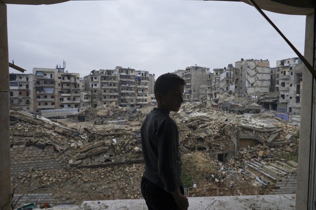 In this picture taken Sunday, Jan. 21, 2018, Hamza Sabbagh checks the destruction from his home balcony that damaged by shelling in Aleppo, Syria. Thirteen months after government forces captured eastern rebel-held neighborhoods of Aleppo, life in the city has improved drastically with more security and more supplies of water and electricity. (AP Photo/Mstyslav Chernov)