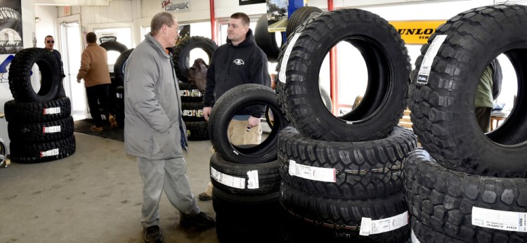 Waterville Tire Warehouse Manager Mike Savage, right, speaks with customer Dan Bernier on Tuesday at the busy company in Waterville. Savage said the recent cold weather has caused a spike in the company's tire repair business.