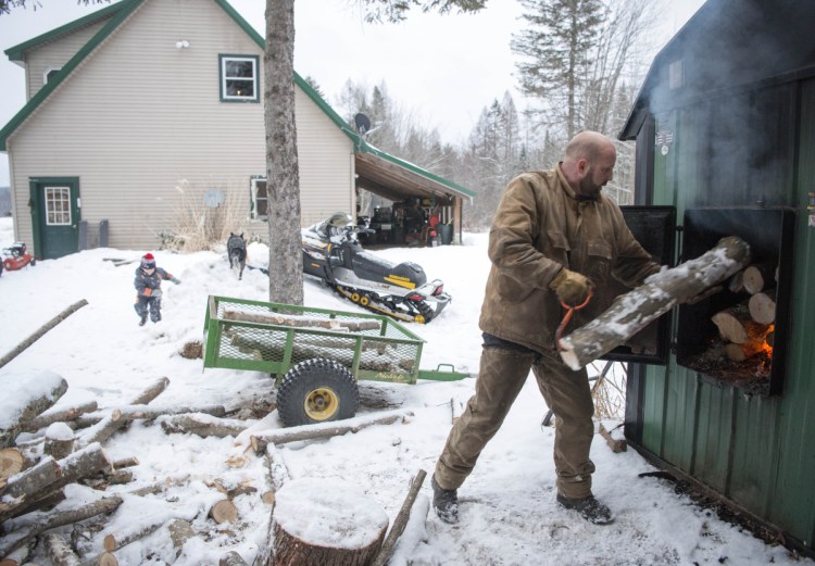 James Black loads logs into his wood-burning furnace, the main heating source for his home in Wilton. Black also has a wood lot with timber he has made available on an emergency basis.