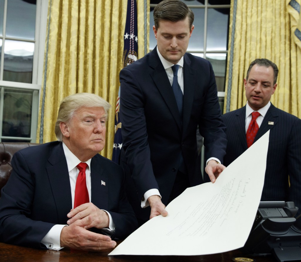 In this Jan. 20, 2017 file photo, White House Staff Secretary Rob Porter, center, hands President Donald Trump a confirmation order for James Mattis as defense secretary, in the Oval Office of the White House in Washington, as White House Chief of Staff Reince Priebus, right, watches.  Porter is stepping down following allegations of domestic abuse by his two ex-wives.
