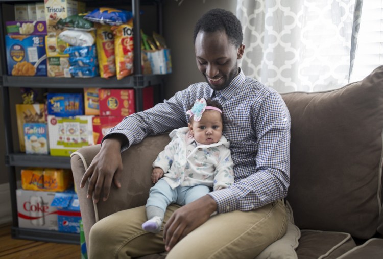Douglas Rutamu and his 4-month-old daughter, Zahra, at their home in Portland. Rutamu and his partner, Jessica Morse, started the delivery service Snacks on Snacks in January. The service mostly delivers candy, but can also bring items like diapers and formula.